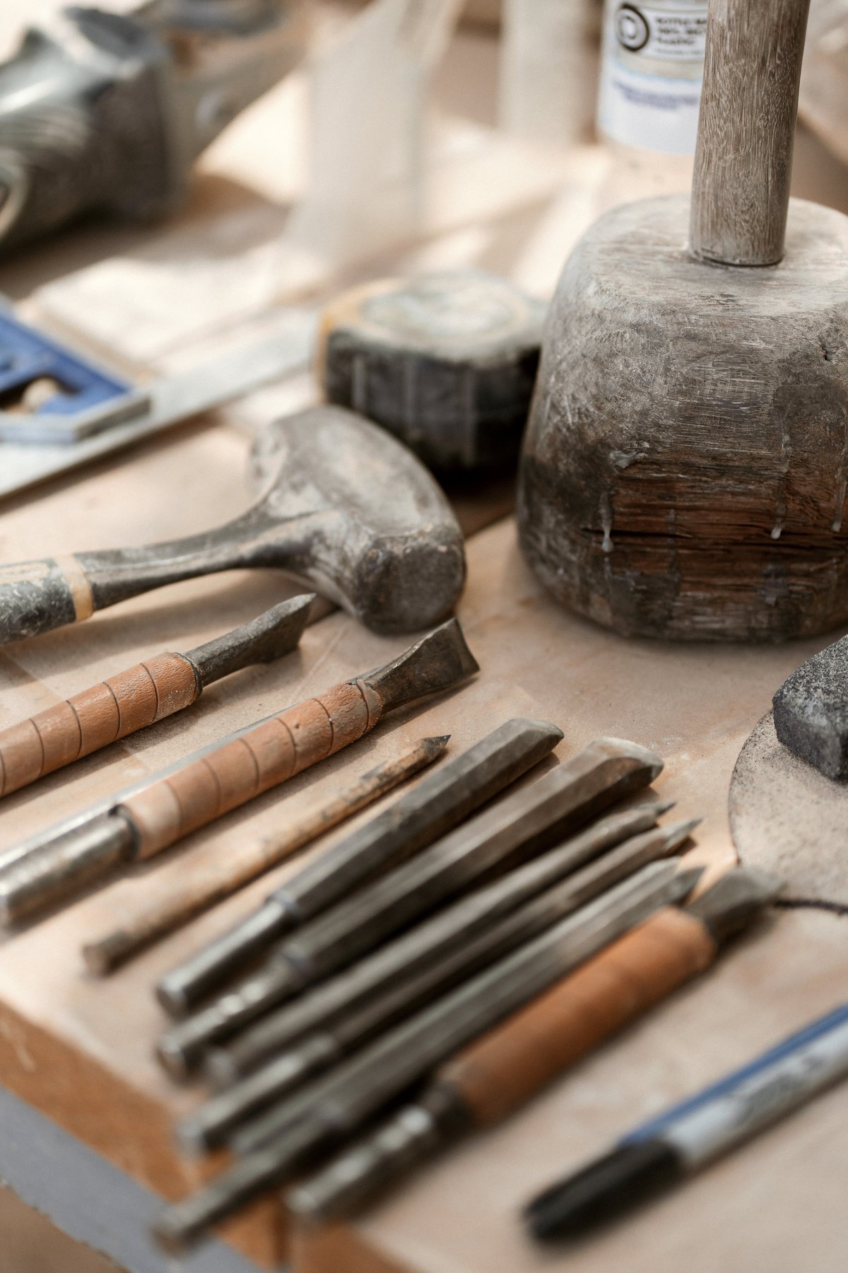 Collection of woodworking and stone carving tools including chisels, hammers, and mallets arranged on a work surface