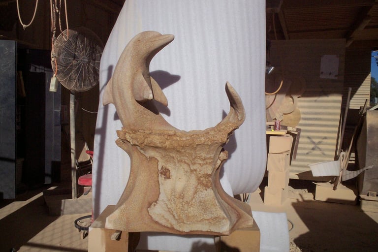 Wooden carved sculpture of a crescent moon face with curved features displayed on a base in an art studio or workshop setting