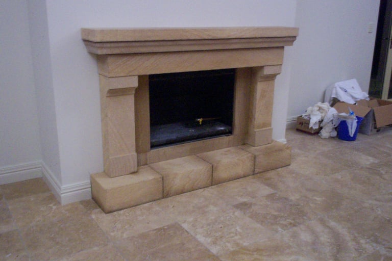Beige stone fireplace with dark interior opening and brick hearth in interior room under construction