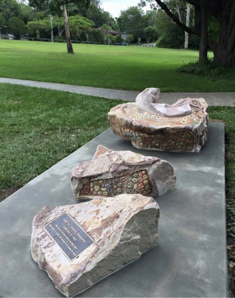 Three carved stone sculptures displayed on concrete platform in a park with green lawn and trees in background
