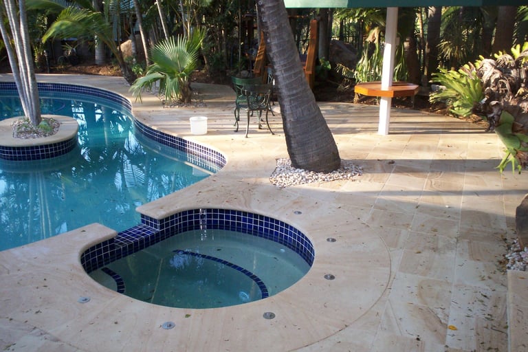 Tropical backyard with curved swimming pool and circular spa, surrounded by palm trees and lounge furniture
