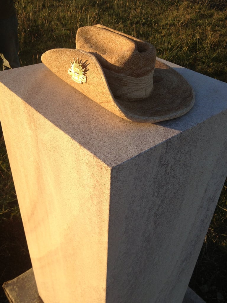 Cowboy hat displayed on a concrete pedestal with a small daisy flower tucked in the band