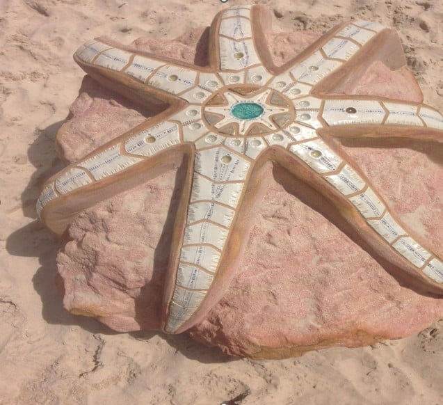 Decorative starfish sculpture with geometric patterns and turquoise center on sandy beach
