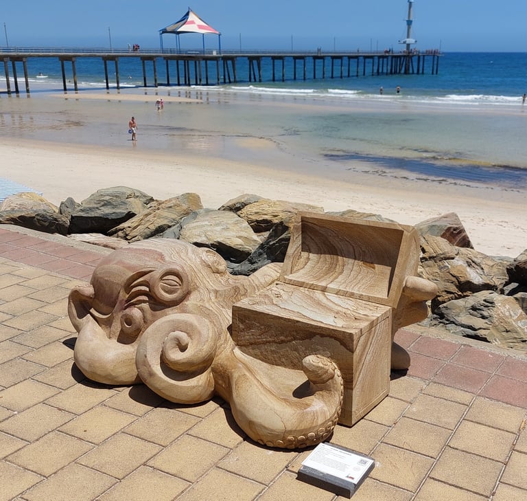 Wooden octopus sculpture on beach boardwalk with pier and sandy beach in background