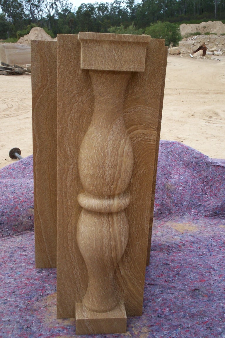 Hand-carved wooden post with decorative relief sculpture on sandy ground with purple mulch and trees in background