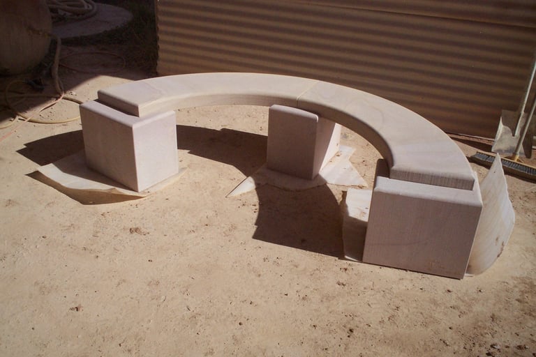 Concrete bench seating with curved backrest sections arranged in a U-shape on sandy ground