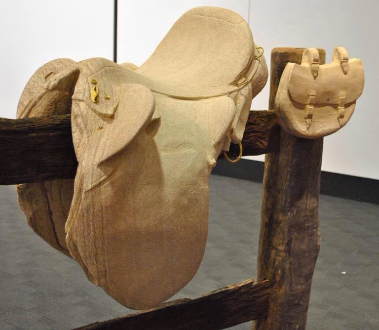 Wooden western saddle displayed on a wooden stand in an indoor gallery setting