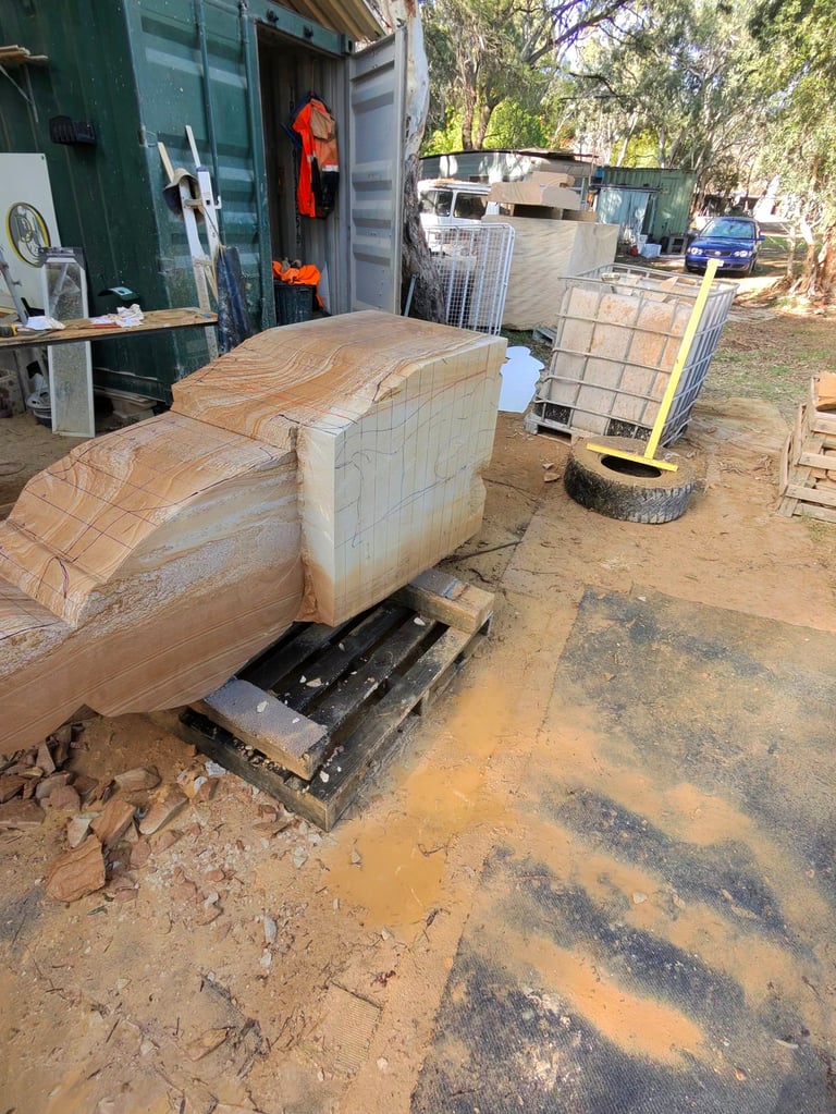 Large wooden boat hull under construction in outdoor workshop with shipping containers and tools visible in background