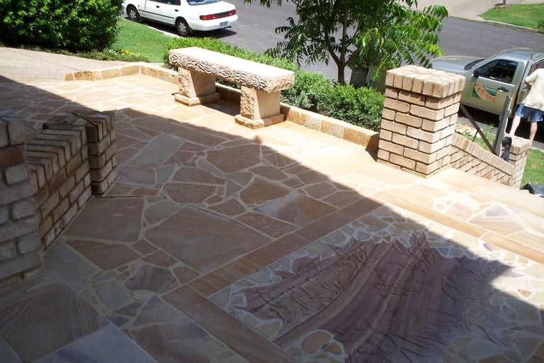 Aerial view of a residential patio under construction with decorative stone pavers, brick pillars, and a bench structure