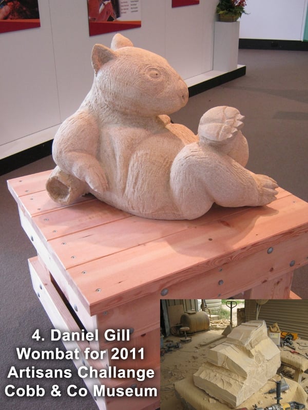 Carved wooden wombat sculpture on pink wooden platform, gallery setting, labeled as Daniel Gills 2011 Artisans Challenge entry