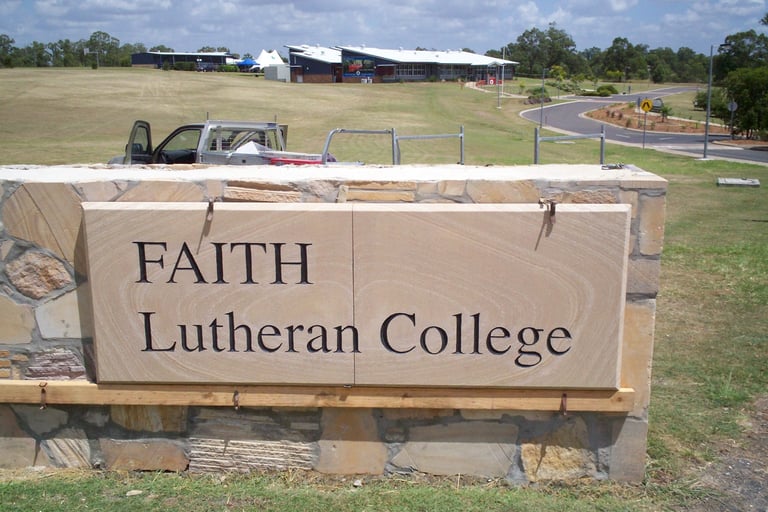 FAITH Lutheran College entrance sign with pastoral campus landscape and farm buildings in the background