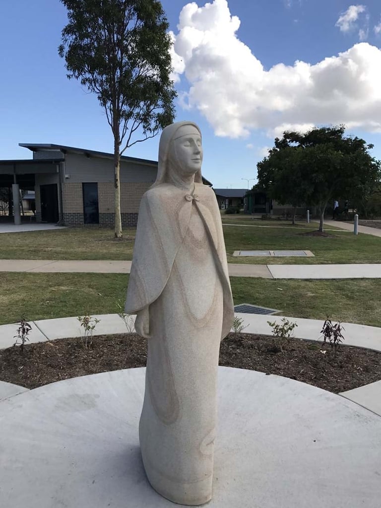 Stone statue of a standing female figure in a public garden with buildings and trees in the background