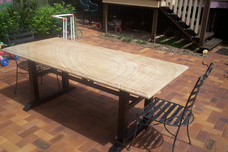 Large wooden outdoor dining table on brick patio with decorative metal chairs and shed in background