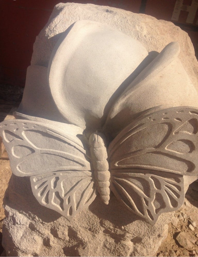 Stone relief sculpture of a butterfly emerging from or perched on a curved, shell-like flower form
