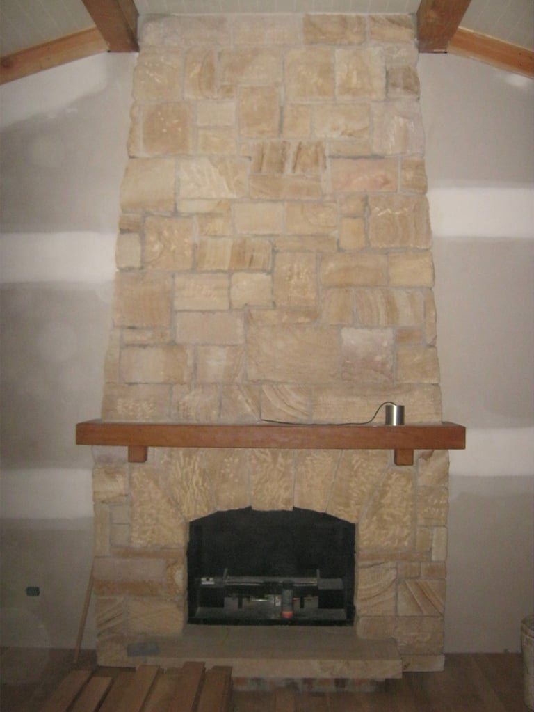 Beige stone fireplace with dark firebox opening and wooden mantel in living room