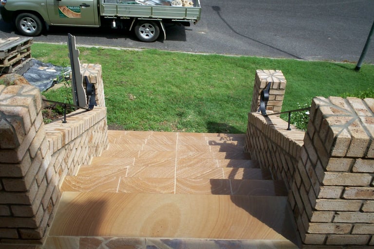 Aerial view of a wet concrete patio under construction surrounded by brick walls, with green lawn and a parked truck visible