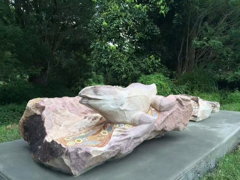 Stone alligator sculpture displayed on a platform with green trees in the background